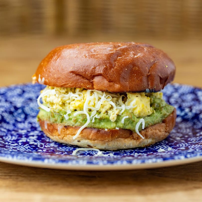 Cafe Crewy's breakfast sandwich with scrambled eggs, guacamole, and shredded cheese on a brioche bun.