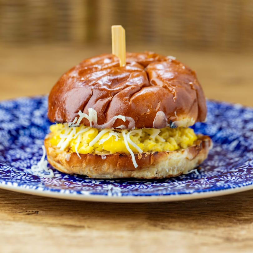 A Cafe Crewy breakfast sandwich with scrambled eggs and cheese on a brioche bun.