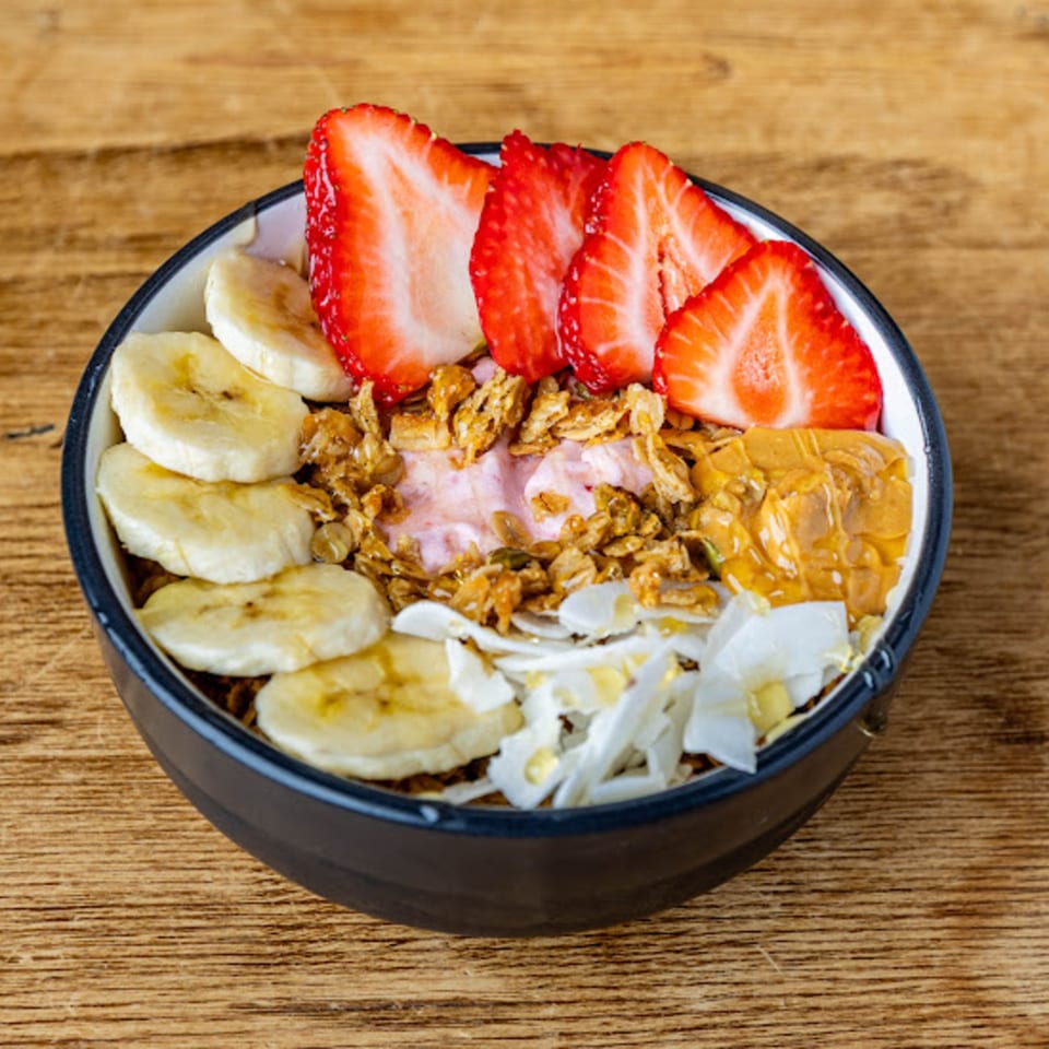 A colorful Cafe Crewy smoothie bowl with strawberries, bananas, granola, peanut butter, and coconut flakes.