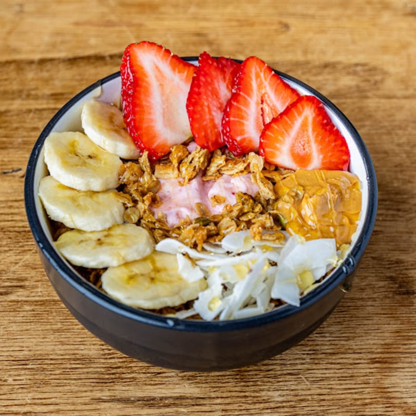 A colorful Cafe Crewy smoothie bowl with strawberries, bananas, granola, peanut butter, and coconut flakes.