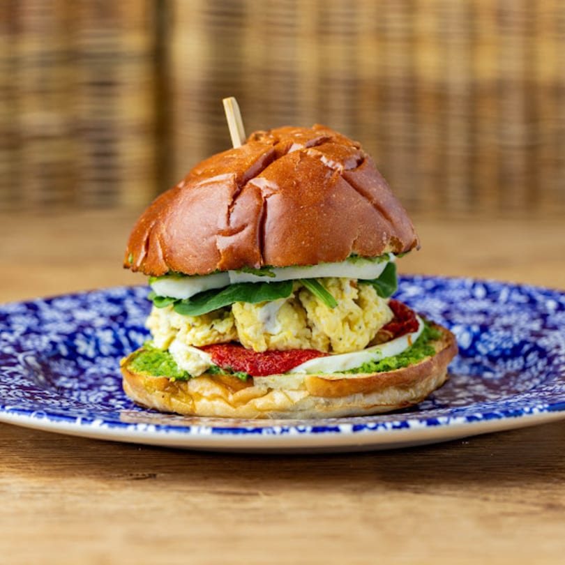 A Cafe Crewy breakfast sandwich with scrambled eggs, pesto, and sun-dried tomatoes on a blue plate.