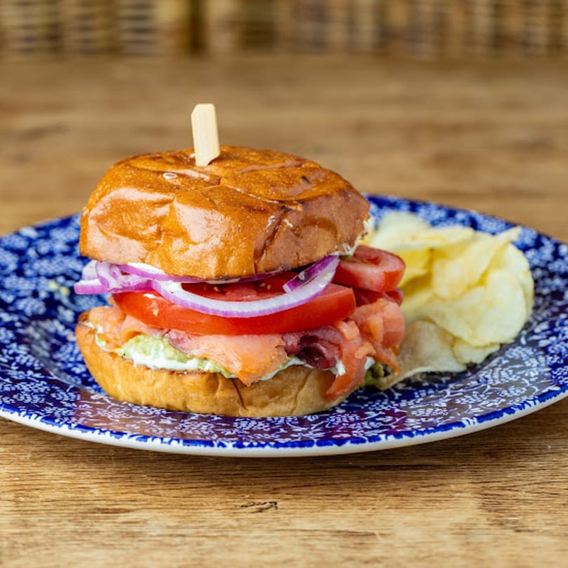 Cafe Crewy's salmon sandwich with red onion, tomato, and chips on a blue and white plate.