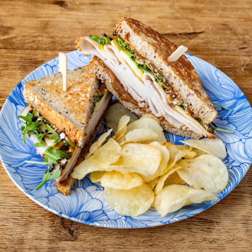 Turkey sandwich with arugula, cheese, and balsamic glaze, served with potato chips on a blue plate.