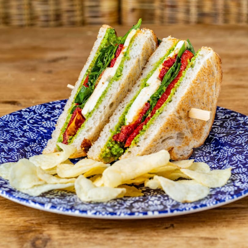 A pesto, mozzarella, and sun-dried tomato sandwich with chips on a blue and white plate.