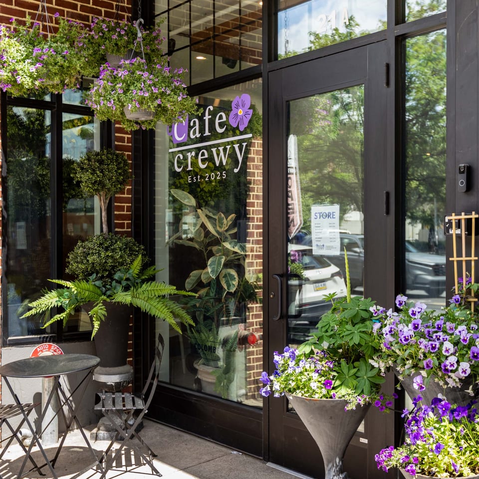 Cafe Crewy's storefront with outdoor seating, hanging purple flowers, and potted plants.