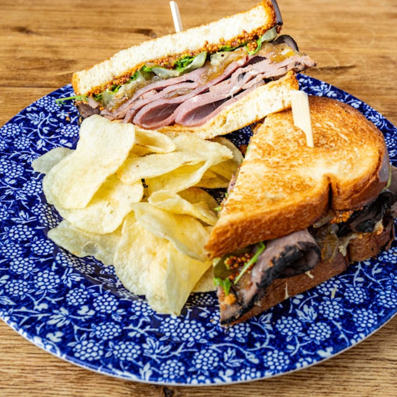 A roast beef sandwich with mustard and lettuce, served with potato chips on a blue and white plate.
